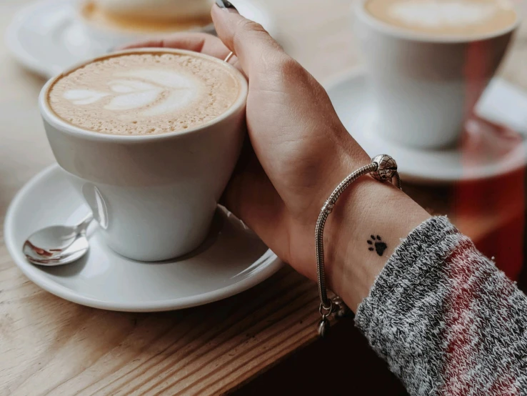 a close up of a person holding a cup of coffee, by Julia Pishtar, trending on pexels, wearing two silver bracelets, cafe for felted animals, arms covered in gang tattoo, best friends