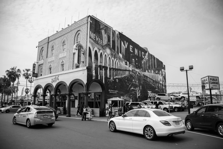 a black and white photo of a city street, a black and white photo, pexels contest winner, art nouveau, drive in movie theater, painted on a giant wall, caulfield, cars and people