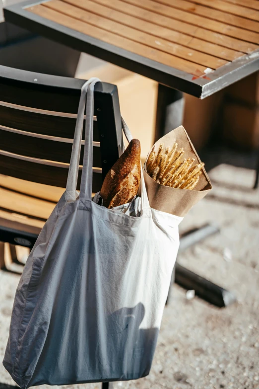 a bag full of bread sitting on top of a wooden table, pexels contest winner, plasticien, shopping groceries, al fresco, grey, inside a french cafe