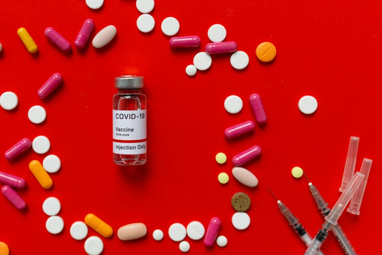 a bottle of medicine sitting on top of a red surface, inspired by Damien Hirst, trending on pexels, vibrant vials, poster of corona virus, candy treatments, syringe