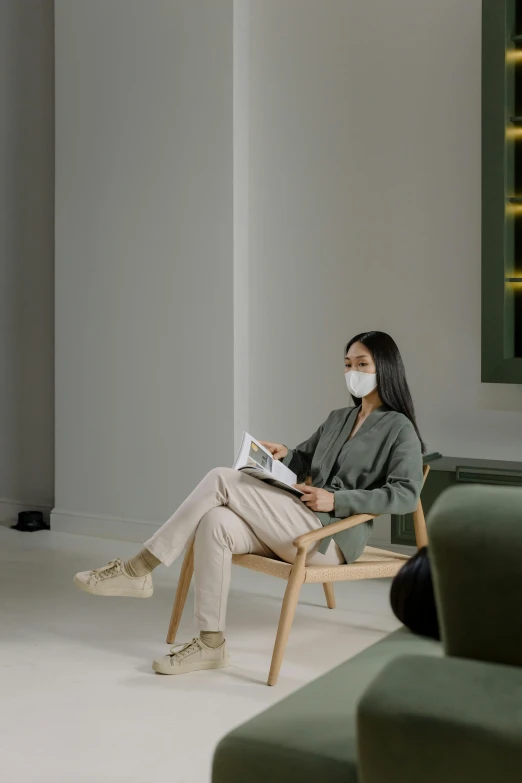 a woman sitting in a chair with a laptop, visual art, medical mask, contemporary aesthetic, beige, waiting room