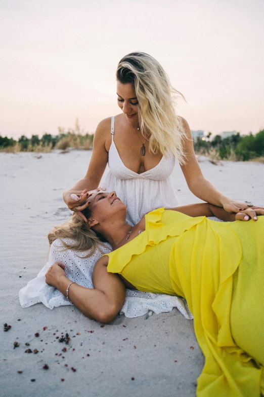 a woman laying on top of a man on a beach, a photo, unsplash, lady using yellow dress, a blond, lesbians, motherly