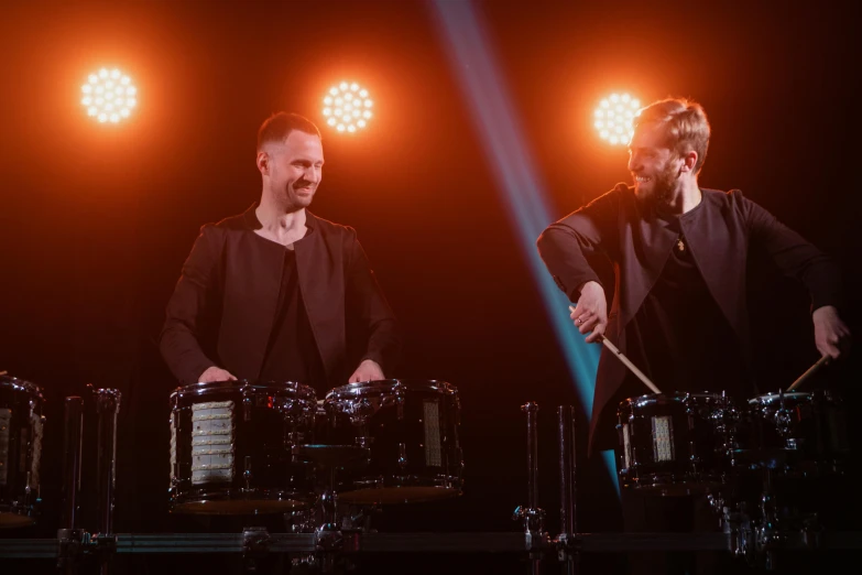 a couple of men standing next to each other on a stage, a portrait, by Julia Pishtar, shutterstock, playing drums, james gurney and andreas rocha, twins, 15081959 21121991 01012000 4k