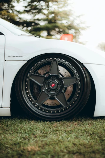 a white car parked on top of a lush green field, a picture, by Austin English, unsplash, renaissance, black wheel rims, full body extreme closeup, hsv, made of swiss cheese wheels
