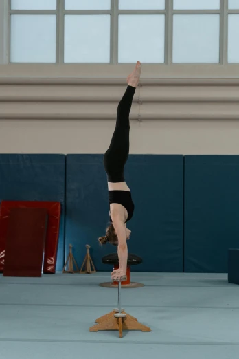 a person doing a handstand on a pole in a gym, inspired by Elizabeth Polunin, arabesque, hexagonal shaped, cardboard, spire, image