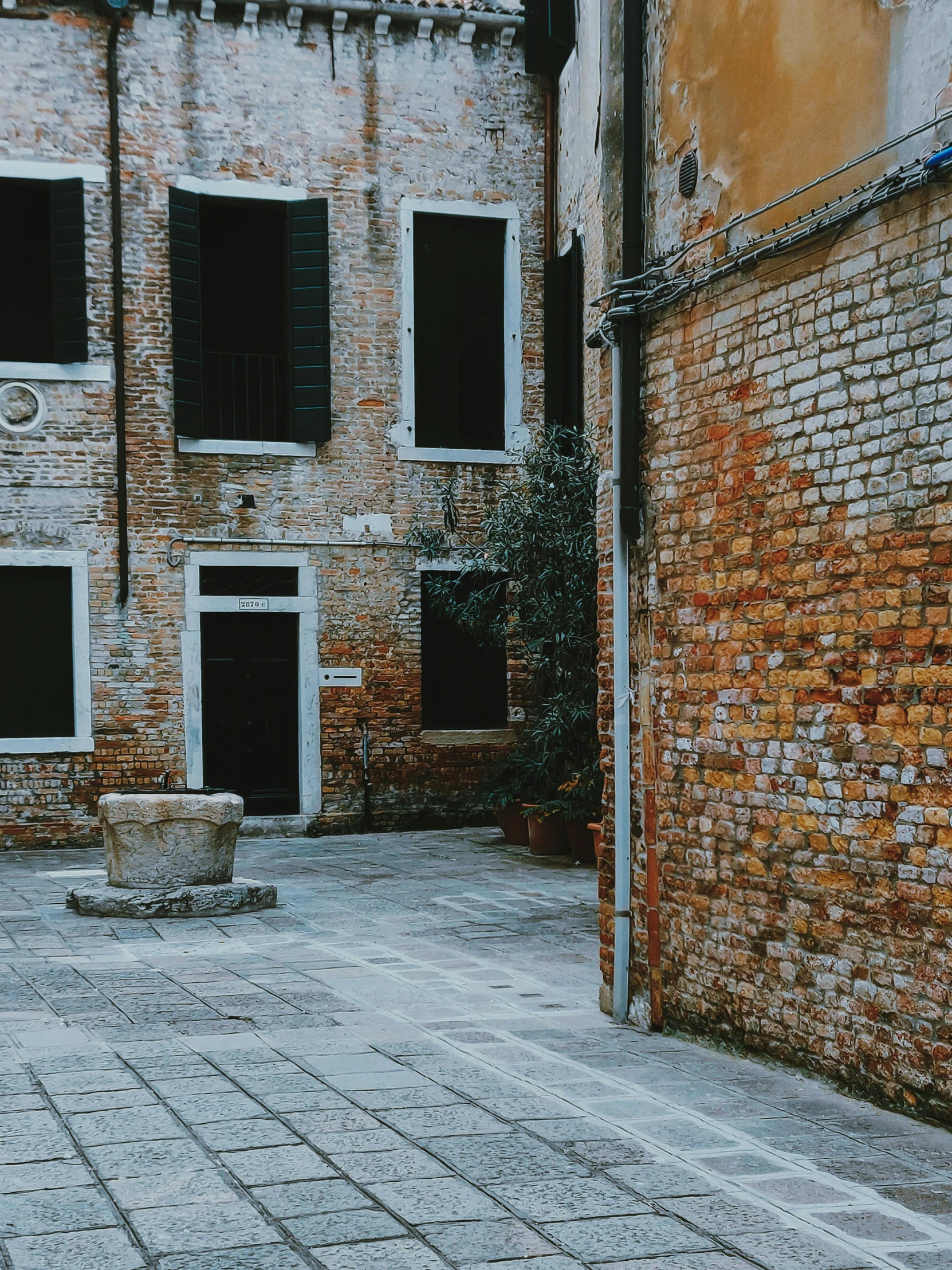 a red fire hydrant sitting on the side of a brick building, inspired by Quirizio di Giovanni da Murano, pexels contest winner, empty streetscapes, a wide open courtyard in an epic, ruins around, parce sepulto