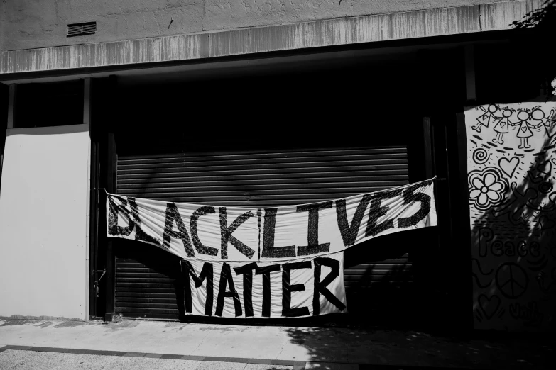 a black and white photo of a banner in front of a garage, a black and white photo, by Meredith Dillman, black arts movement, black skin!!!, alive, background image, matter