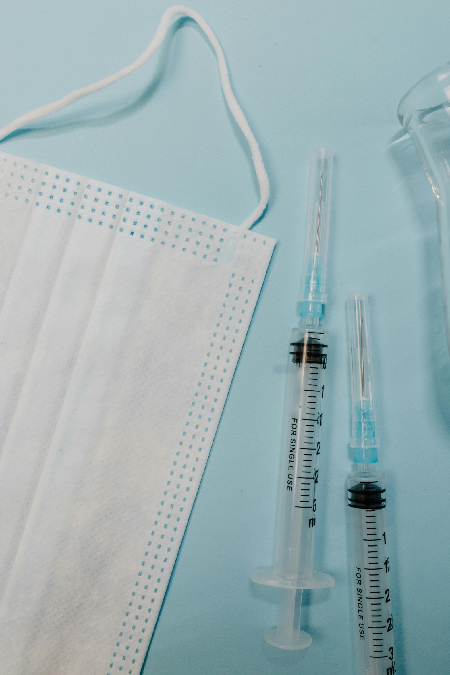 a medical mask, syos and a bottle on a blue background, a picture, by Ryan Pancoast, shutterstock, syringes, 1 6 x 1 6, on a pale background, made of lab tissue