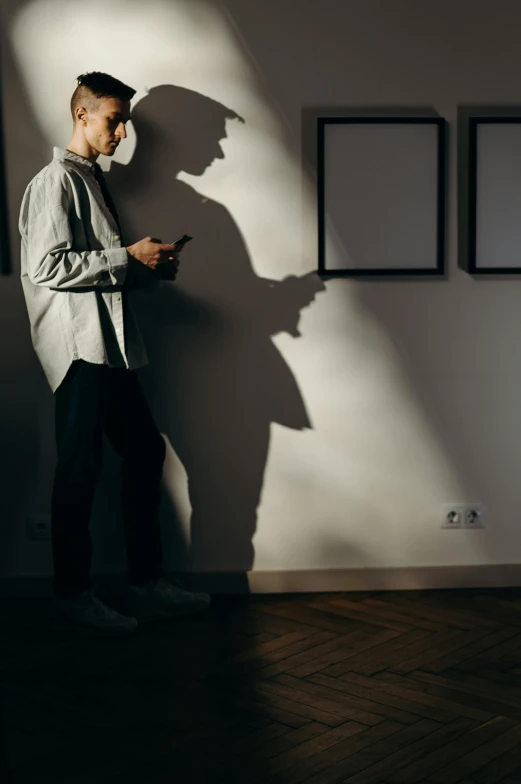 a man leaning against a wall using a cell phone, a poster, trending on pexels, visual art, faces covered in shadows, at home, long shadow, masked person in corner