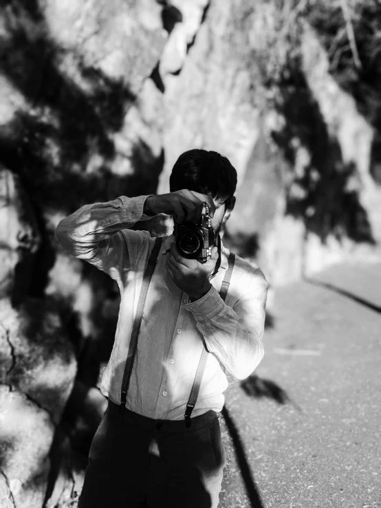 a man taking a picture of himself with a camera, a black and white photo, inspired by Sergio Larraín, high contrast dappled lighting, against the backdrop of trees, marble!! (eos 5ds r, photographed on colour film