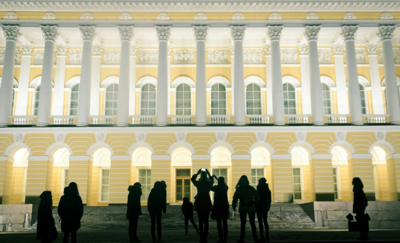 a group of people standing in front of a building, by Serhii Vasylkivsky, pexels contest winner, academic art, yellow lighting, russian neoclassicism, square, college