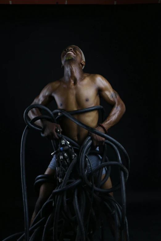 a man sitting on top of a pile of wires, an album cover, inspired by Candido Bido, hyperrealism, body building blacksmith, hoses:10, black main color, photos