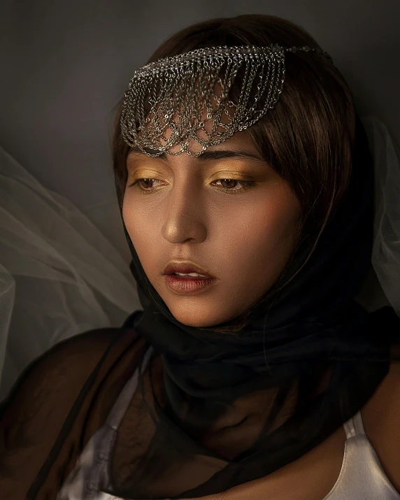 a close up of a woman wearing a veil, inspired by irakli nadar, asian descent, draped in shiny gold and silver, non binary model, with a sad expression
