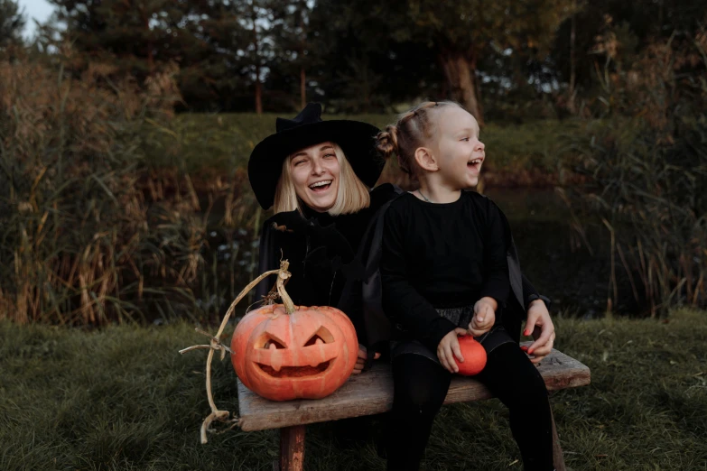 a couple of kids sitting on top of a wooden bench, by Emma Andijewska, pexels contest winner, beautiful witch spooky female, both laughing, gif, wearing black old dress and hat