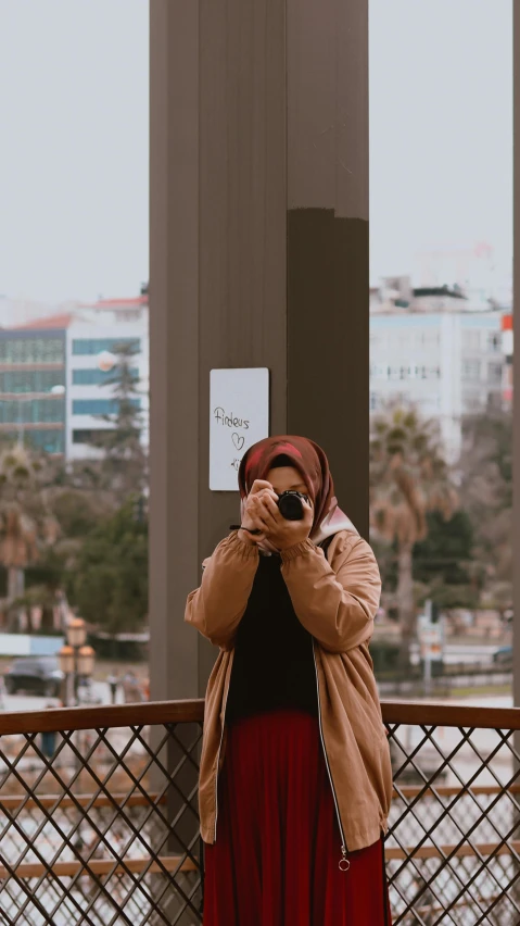 a woman taking a picture of herself with a camera, by Ismail Acar, pexels contest winner, visual art, hijab, looking outside, low quality photo, casual pose