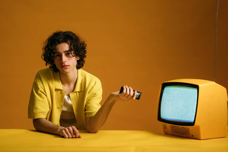 a woman sitting at a table in front of a television, trending on pexels, fantastic realism, wavy hair yellow theme, teenage boy, posing for a picture, vhs style