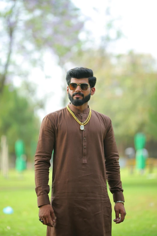 a man standing on top of a lush green field, by Max Dauthendey, pexels contest winner, hurufiyya, he is wearing a brown sweater, wearing gold jewellery, ( ( theatrical ) ), square