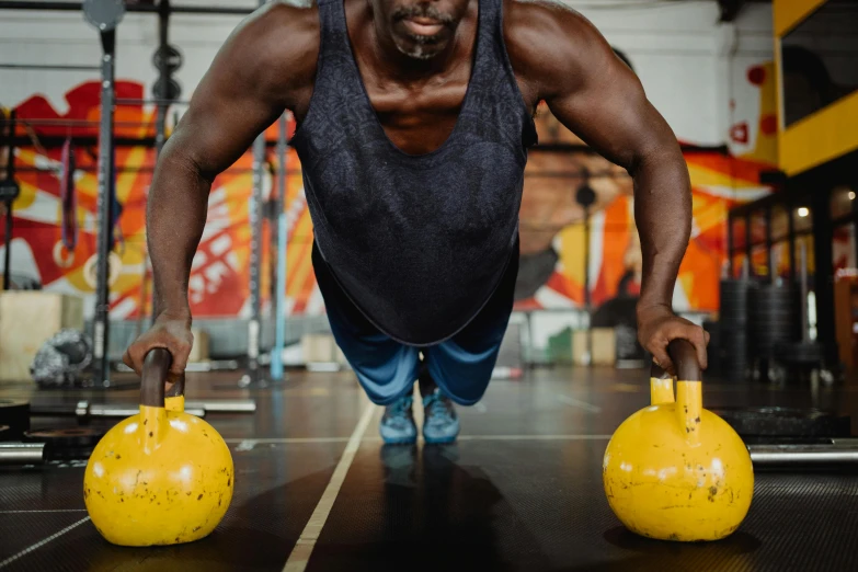 a man doing push ups with kettlebells in a gym, by Lee Loughridge, pexels contest winner, wearing yellow croptop, black man, 🦩🪐🐞👩🏻🦳, round-cropped