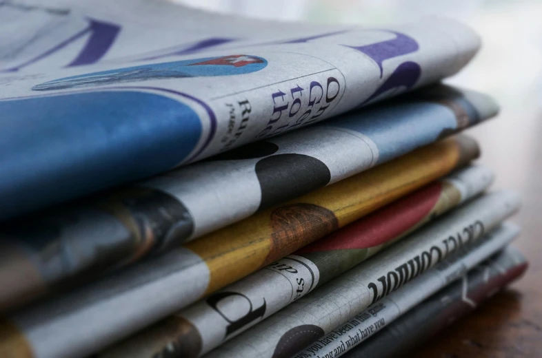 a stack of newspapers sitting on top of a wooden table, a picture, pexels, private press, multi - coloured, panels, fim still, middle close up