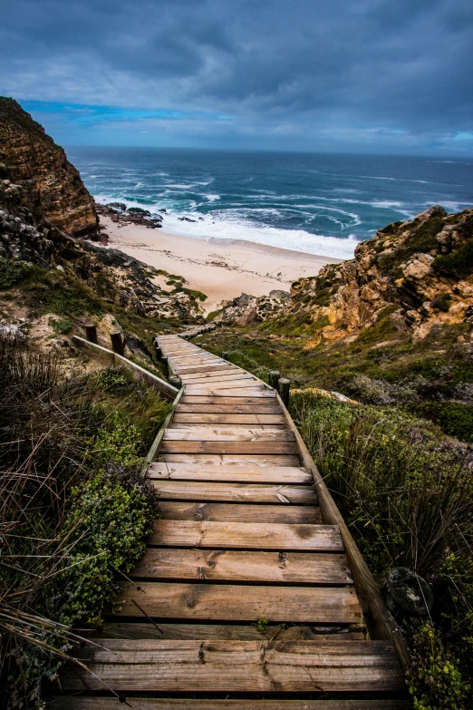 a wooden path leading to a beach on a cloudy day, by Daniel Seghers, pexels contest winner, 2 5 6 x 2 5 6 pixels, large staircase, south african coast, steep cliffs