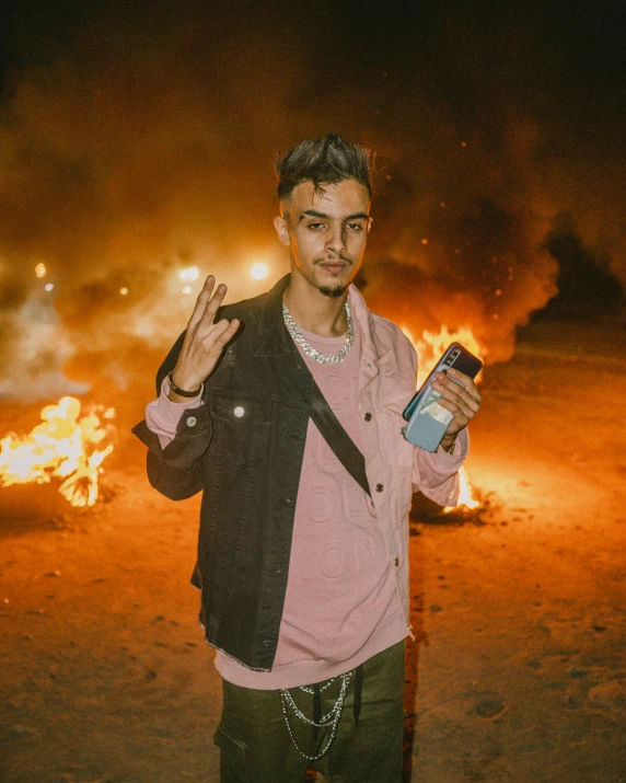 a man that is standing in front of a fire, an album cover, trending on unsplash, graffiti, holding a bottle of arak, non binary model, in desert, playboi carti portrait