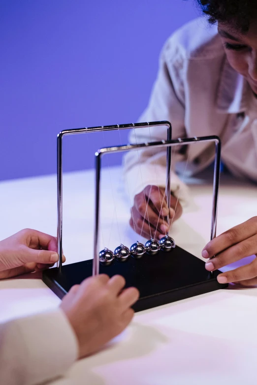 a couple of people sitting at a table with a newton newton newton newton newton newton newton newton newton newton newton newton newton newton newton newton newton newton, a hologram, pexels contest winner, kinetic art, newton's cradle, fully in frame, dynamic action shot, 2 - minute tabletop