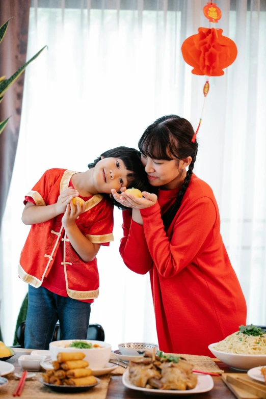 a couple of women standing in front of a table filled with food, wearing a red cheongsam, kids, profile image, holding a tangerine