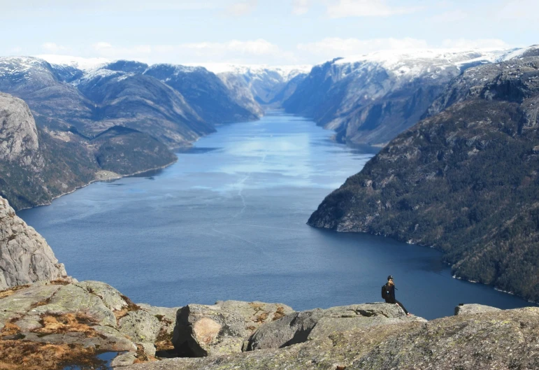 a person standing on top of a mountain next to a body of water, by Tom Wänerstrand, pexels contest winner, hurufiyya, fjords in background, hyperdetailed, targ nar, view from high