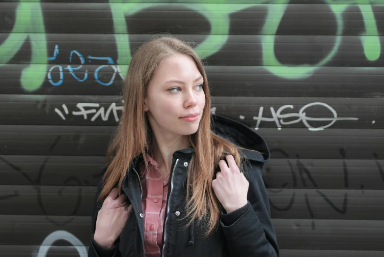 a woman standing in front of a graffiti covered wall, inspired by Louisa Matthíasdóttir, pexels contest winner, wearing a black jacket, portrait sophie mudd, plain background, pale-skinned