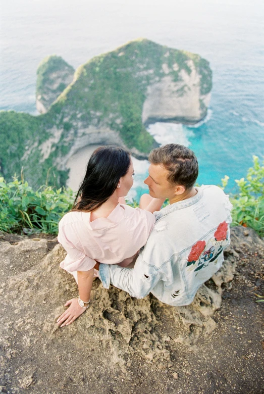 a man and a woman sitting on top of a cliff, bella poarch, flatlay, lush surroundings, coastal cliffs