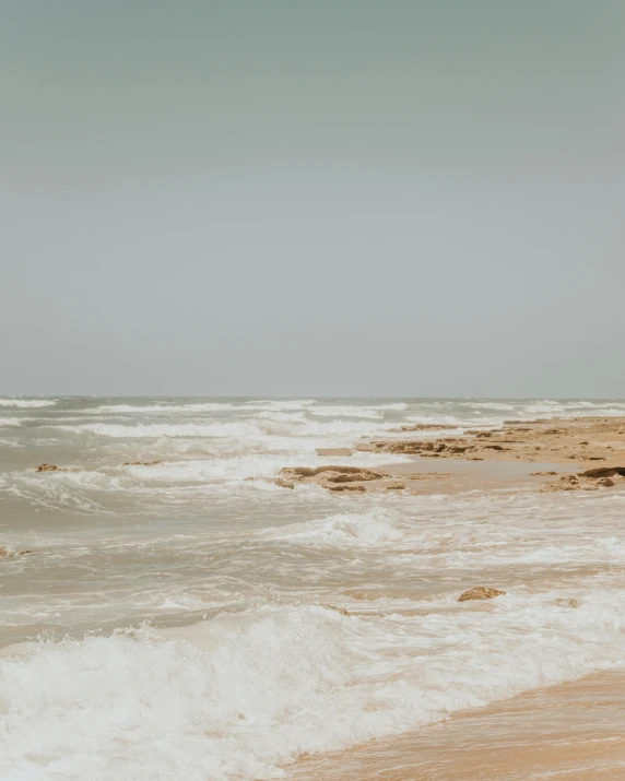 a man standing on top of a sandy beach next to the ocean, pexels contest winner, minimalism, crashing waves and sea foam, sand - colored walls, on a hot australian day, a photo of the ocean