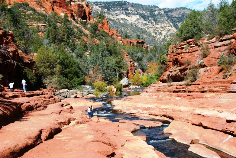 a man standing on top of a rock next to a river, red sandstone natural sculptures, quintessa, river running through it, promo image