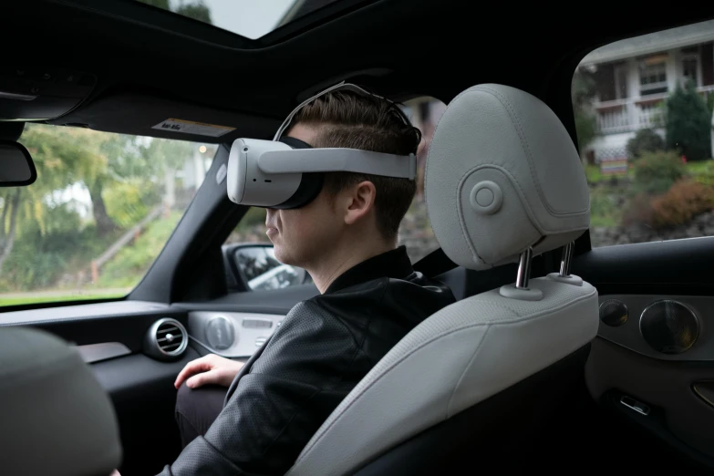 a man in a car wearing a virtual reality headset, inspired by An Gyeon, a wide shot, rear-shot, looking across the shoulder, looking left