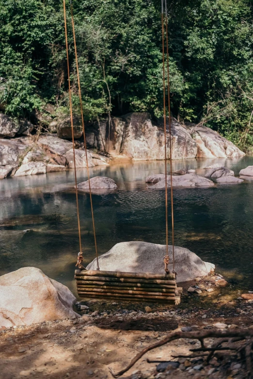 a wooden swing hanging over a body of water, sumatraism, streams and rocks, next to a small river, rock pools, retro vibe