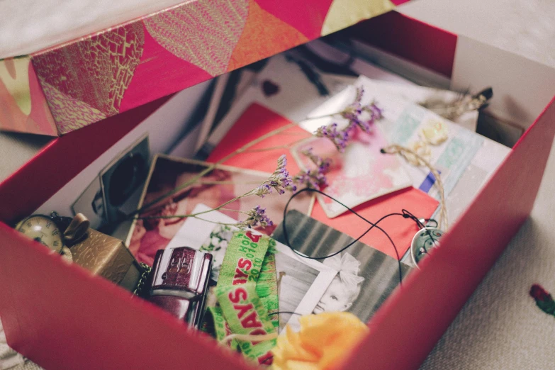 a box filled with assorted items sitting on top of a bed, pexels contest winner, mail art, purple and scarlet colours, close up half body shot, sentimental, ribbon