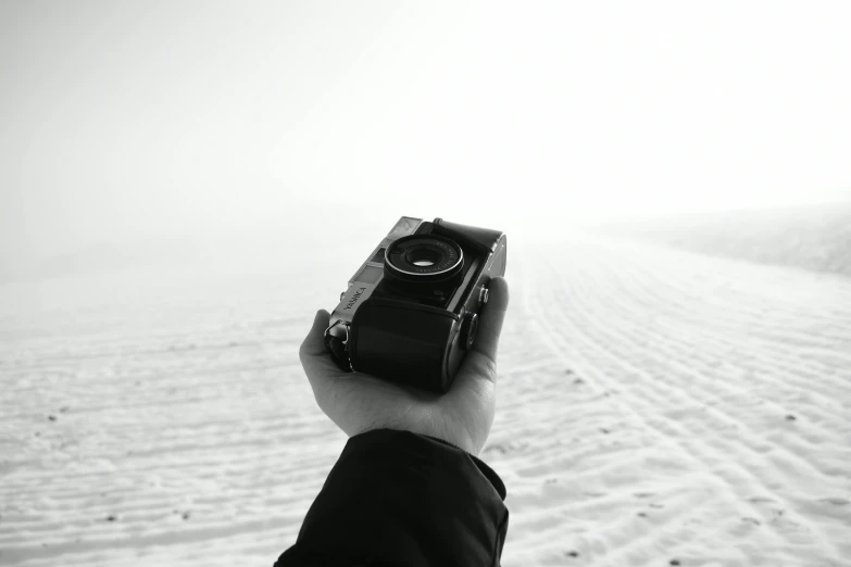 a person holding a camera in the snow, a black and white photo, white desert, 4k photography high quality, minimalistic aesthetics, cinematic outfit photo