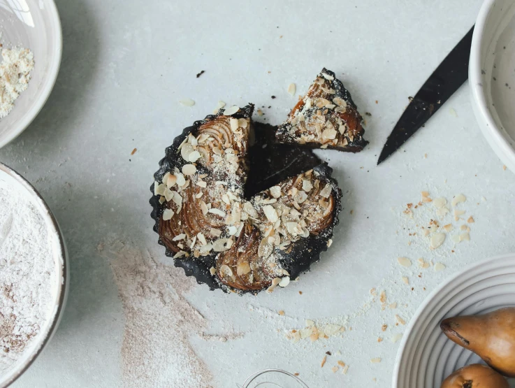 a cake sitting on top of a table next to bowls of food, inspired by Richmond Barthé, unsplash, hurufiyya, licorice allsort filling, crust, on a pale background, rusty