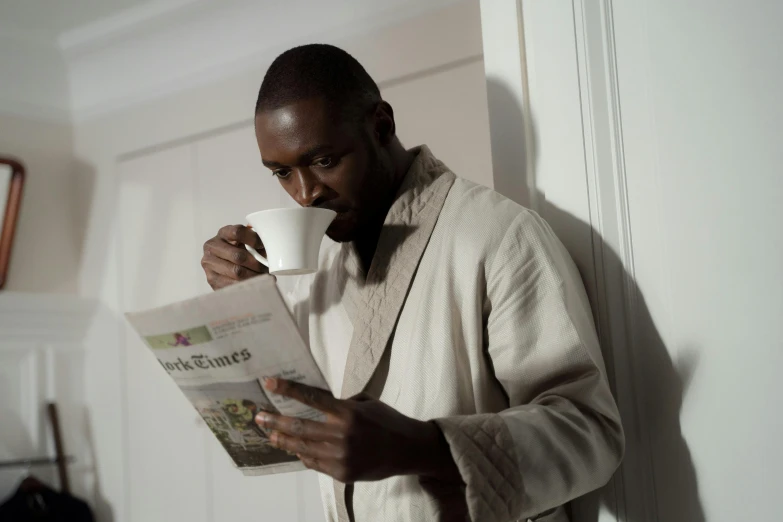 a man reading a newspaper and drinking a cup of coffee, inspired by Rajmund Kanelba, private press, wearing robe, lance reddick, press shot, ap news photograph