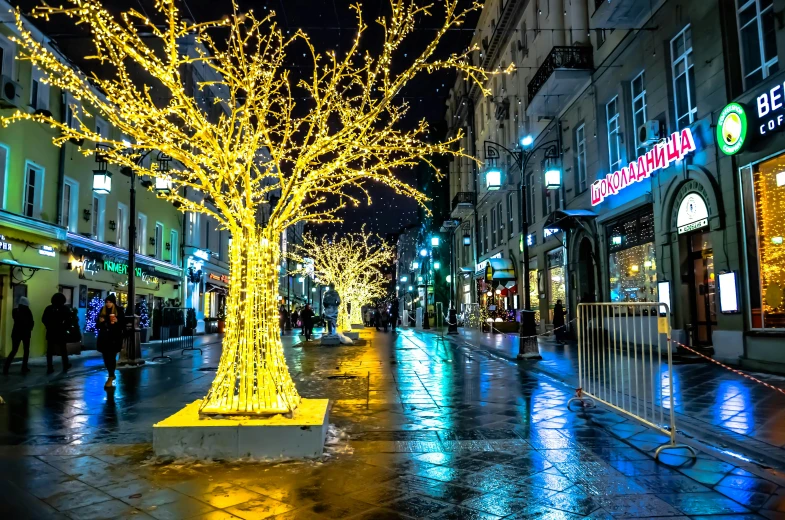 a group of people walking down a street at night, gold decorations, wintertime, wet streets, city lighting