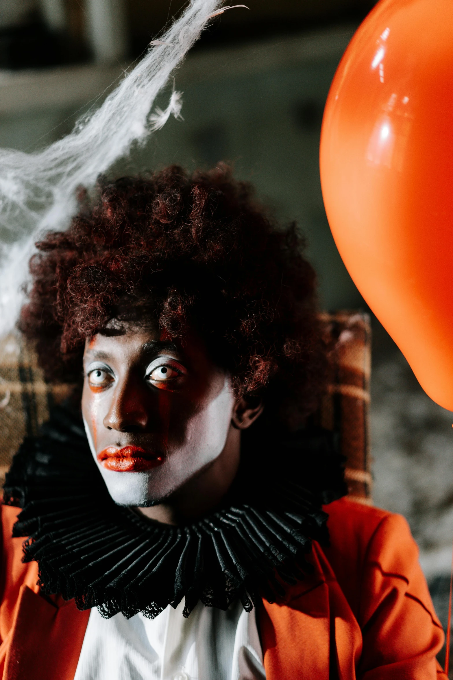 a clown sitting in a chair next to a balloon, a portrait, pexels contest winner, renaissance, with afro, dark grey and orange colours, haunted house themed, actor