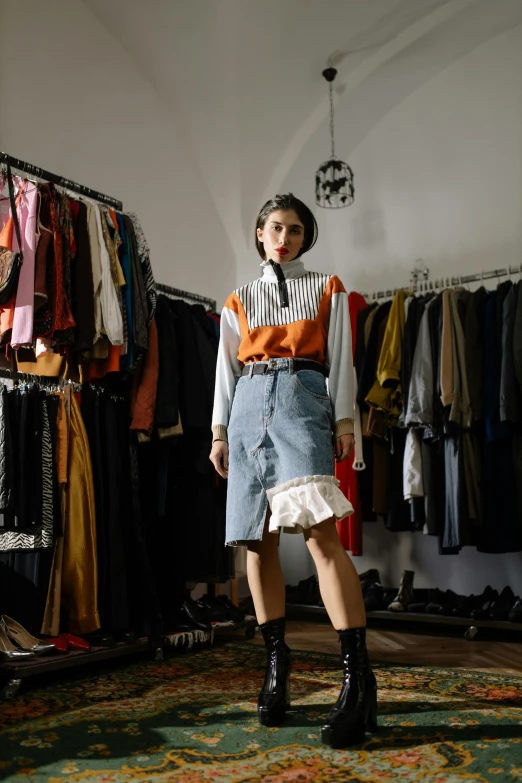 a woman standing in front of a rack of clothes, by Oskar Lüthy, trending on unsplash, renaissance, wearing skirt and high socks, frown fashion model, orange and black tones, wearing a designer top