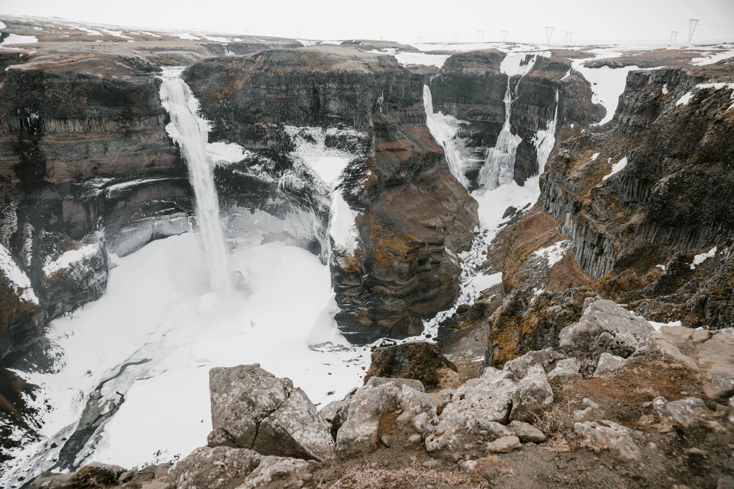 a man standing on top of a cliff next to a waterfall, by Louisa Matthíasdóttir, pexels contest winner, les nabis, snow and ice, multiple waterfalls, looking down at a massive crater, chriss foss