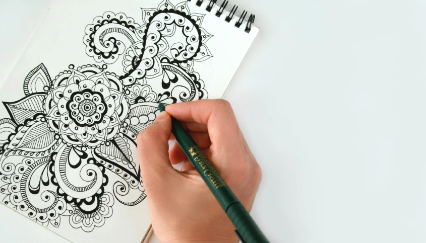 a person is drawing on a piece of paper, a detailed drawing, inspired by artist, intricate paisley filigree, felt tip pen, intricate details. front on, stylised design