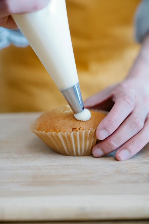 a person putting icing on a cupcake on a cutting board, by Matthias Stom, unsplash, kek, cone shaped, cream, tall