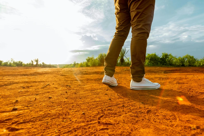 a man standing on top of a dirt field, by Julian Allen, pexels contest winner, gum rubber outsole, on a hot australian day, unmistakably kenyan, warm glow coming the ground