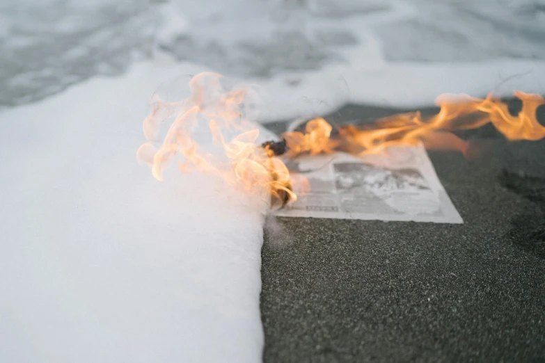 a newspaper sitting on top of a beach covered in snow, an album cover, unsplash, auto-destructive art, casting a flame spell, sidewalk, on white paper, close-up photograph