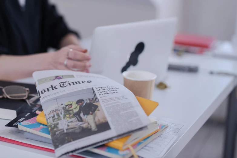 a woman sitting at a desk in front of a laptop computer, a picture, trending on unsplash, private press, in the cover of new york times, on a white table, papers and tomes, foreground background