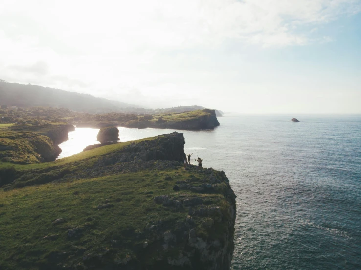 a group of people standing on top of a cliff next to the ocean, marsden, view from the sky, instagram photo, cinematic film still