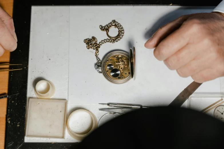 a close up of a person working on a watch, an engraving, trending on pexels, process art, holding a pocket watch, miniature product photo, gold and white, instagram story