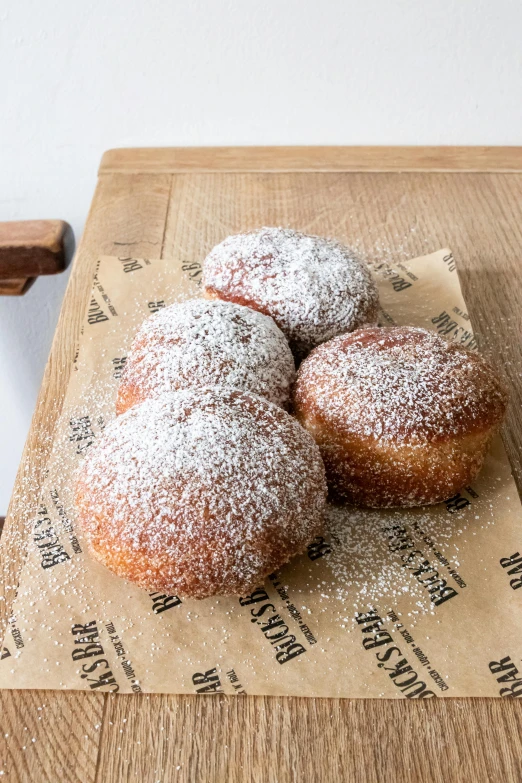 a couple of doughnuts sitting on top of a wooden cutting board, powdered sugar, kreuzberg, 6 pack, buzzed sides